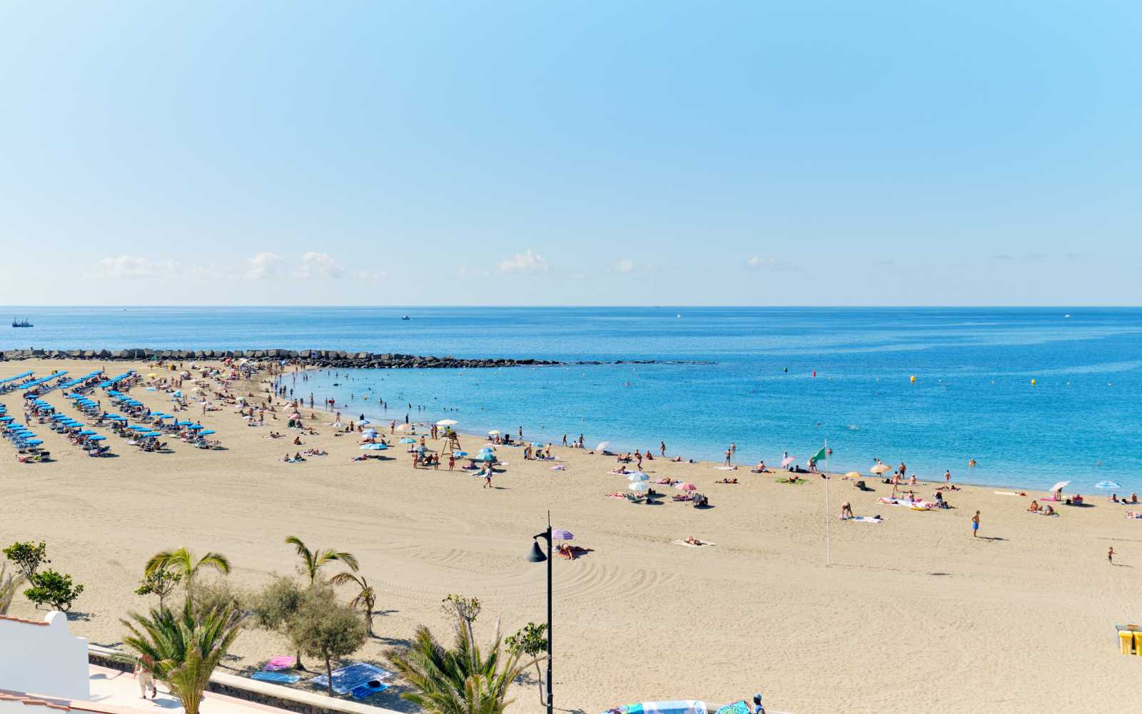 Panoramic view of crowd of people sunbathing on sandy beach of Playa de los Cristianos, enjoy warm weather, Tenerife, Canary Islands, Spain
