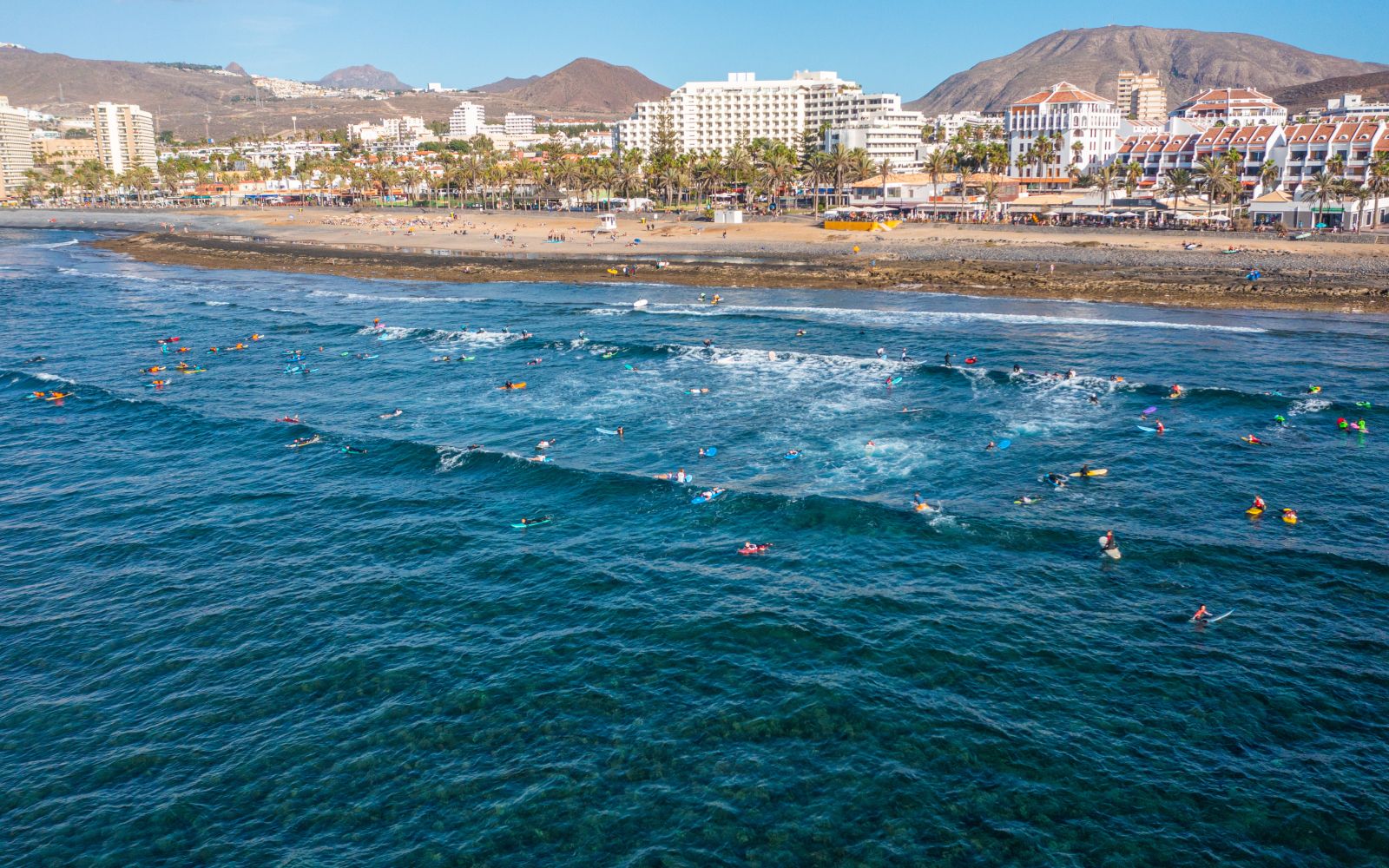 Aerial photo from drone to de surfers in the ocean beachs Adeje Playa de las Americas, Playa Honda In the background Tenerife at sunset. Tenerife, Canary islands, Spain